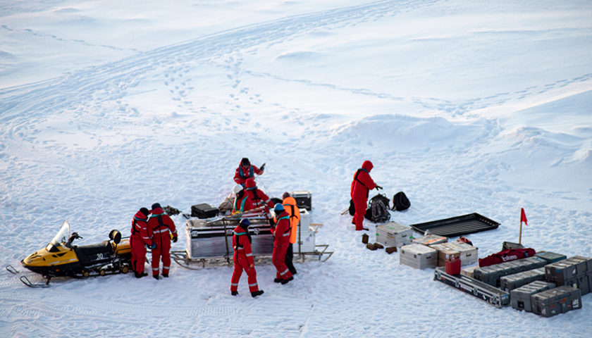 expédition scientifique de 7 hommes en rouge et un homme en orange inspectant des grosses caisses de matériels